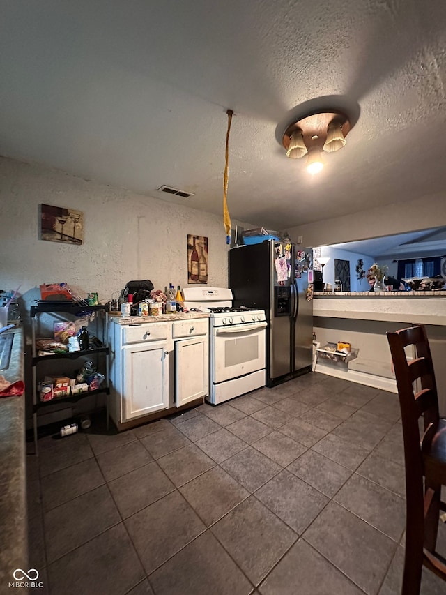 4607 Melrose Ave, Indianapolis, IN 46241 - kitchen with gas range gas stove, stainless steel refrigerator with ice dispenser, dark tile patterned floors, a textured ceiling, and white cabinetry