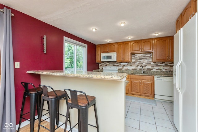 5802 Rymark Ct, Indianapolis, IN 46250 - kitchen featuring white appliances, tasteful backsplash, a breakfast bar, brown cabinets, and light tile patterned flooring