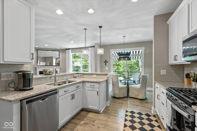 14442 Treasure Creek Ln, Fishers, IN 46038 - kitchen featuring appliances with stainless steel finishes, a peninsula, white cabinets, light wood-style floors, and light stone counters