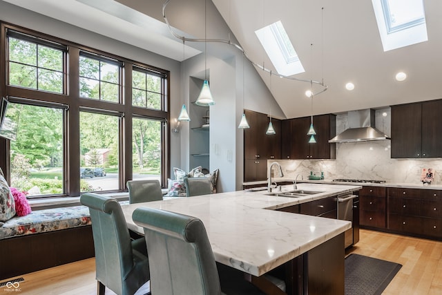 8651 Emerald Ln, Indianapolis, IN 46260 - kitchen featuring wall chimney exhaust hood, a skylight, light stone counters, dark brown cabinets, and light wood-style flooring