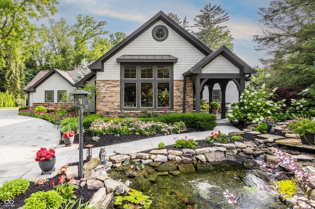 8651 Emerald Ln, Indianapolis, IN 46260 - view of front facade featuring stone siding, a garden pond, and a standing seam roof