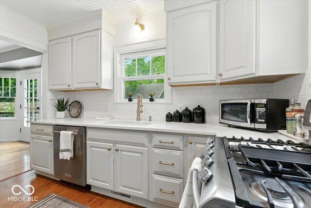 4732 N Kenwood Ave, Indianapolis, IN 46208 - kitchen featuring appliances with stainless steel finishes, wood finished floors, white cabinets, decorative backsplash, and crown molding