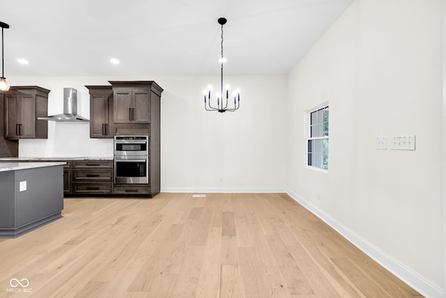 2031 Central Ave, Indianapolis, IN 46202 - kitchen with wall chimney exhaust hood, a chandelier, stainless steel double oven, light wood-style flooring, and dark brown cabinetry