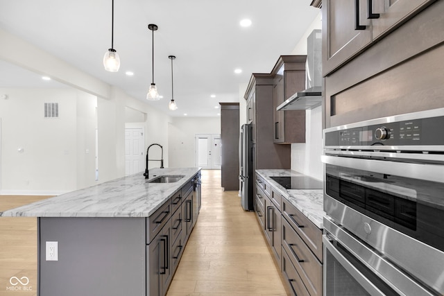 2031 Central Ave, Indianapolis, IN 46202 - kitchen featuring wall chimney range hood, light wood-style flooring, stainless steel appliances, a center island with sink, and recessed lighting