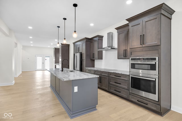 2031 Central Ave, Indianapolis, IN 46202 - kitchen featuring wall chimney range hood, appliances with stainless steel finishes, an island with sink, light wood finished floors, and recessed lighting