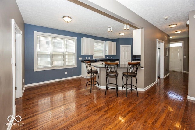 2325 N Talbott St, Indianapolis, IN 46205 - kitchen with dark countertops, white cabinetry, dark wood-type flooring, a kitchen bar, and a textured ceiling