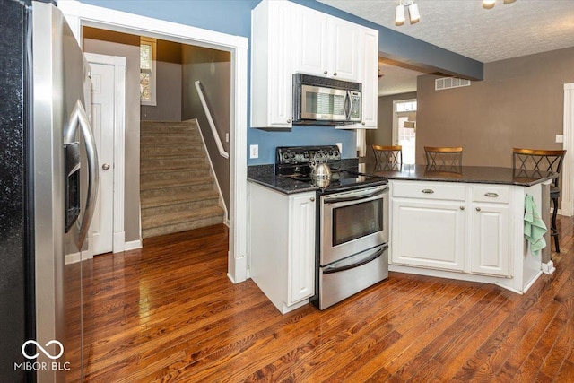 2325 N Talbott St, Indianapolis, IN 46205 - kitchen with appliances with stainless steel finishes, dark wood-style flooring, white cabinetry, a peninsula, and a textured ceiling