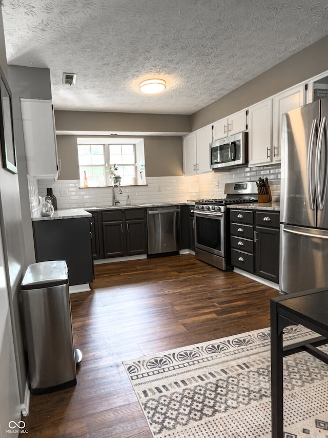 7470 Charrington Ct, Indianapolis, IN 46254 - kitchen featuring stainless steel appliances, white cabinetry, dark wood-type flooring, decorative backsplash, and a textured ceiling