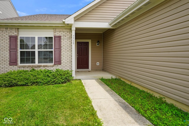 7715 Bolero Dr, Camby, IN 46113 - view of exterior entry with brick siding, a yard, and roof with shingles