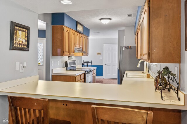 7616 Derrek Pl, Indianapolis, IN 46219 - kitchen with under cabinet range hood, appliances with stainless steel finishes, light countertops, a breakfast bar, and a textured ceiling
