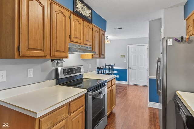 7616 Derrek Pl, Indianapolis, IN 46219 - kitchen with appliances with stainless steel finishes, under cabinet range hood, wood finished floors, light countertops, and brown cabinetry