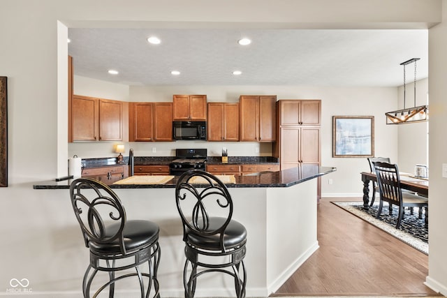 13327 Hockley Dr, Fishers, IN 46037 - kitchen with black appliances, brown cabinets, a breakfast bar, light wood-style floors, and recessed lighting