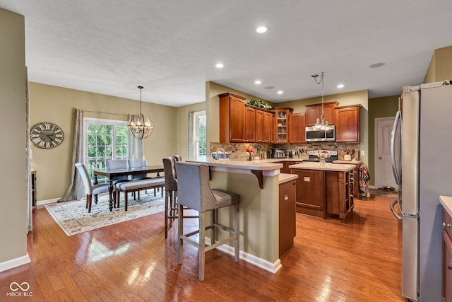 705 Ridge Gate Dr, Brownsburg, IN 46112 - kitchen with stainless steel appliances, a chandelier, glass insert cabinets, a breakfast bar area, and wood-type flooring
