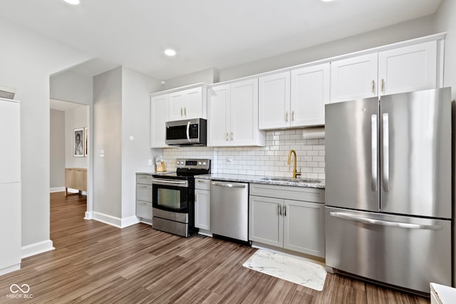 3045 Ruckle St, Indianapolis, IN 46205 - kitchen featuring appliances with stainless steel finishes, wood finished floors, backsplash, white cabinetry, and light stone counters