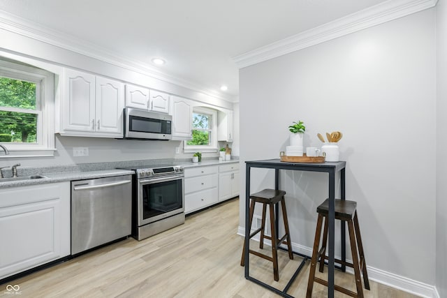 5205 Staughton Dr, Indianapolis, IN 46226 - kitchen with stainless steel appliances, crown molding, white cabinetry, light wood-style floors, and light countertops