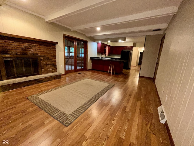 7721 Hollybrook Ln, Indianapolis, IN 46227 - unfurnished living room with wood finished floors, beamed ceiling, a fireplace, french doors, and a textured wall