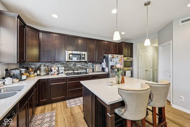 8126 Kilborn Way, Avon, IN 46123 - kitchen featuring appliances with stainless steel finishes, light wood-type flooring, dark brown cabinets, decorative backsplash, and light stone counters