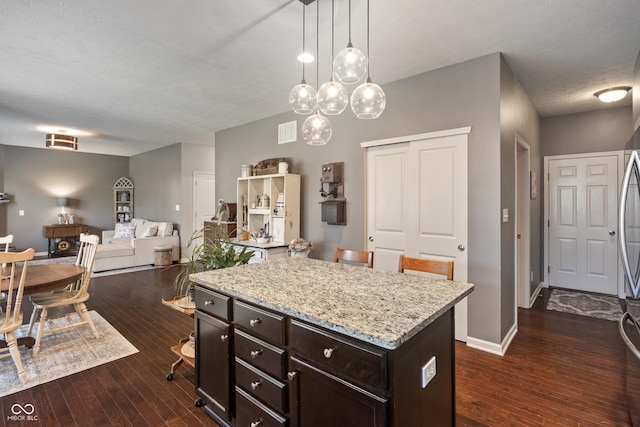 13992 Wynngate Ln, Fishers, IN 46038 - kitchen with a kitchen island, dark wood finished floors, light stone countertops, decorative light fixtures, and dark brown cabinetry