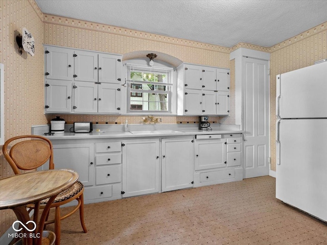 228 W Washington St, Shelbyville, IN 46176 - kitchen featuring wallpapered walls, freestanding refrigerator, light countertops, a textured ceiling, and white cabinets
