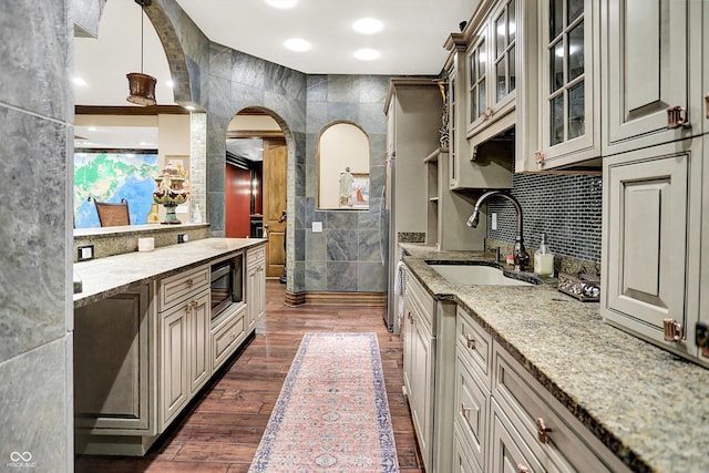 11557 Willow Springs Dr, Zionsville, IN 46077 - kitchen with arched walkways, glass insert cabinets, dark wood-type flooring, stainless steel microwave, and light stone counters