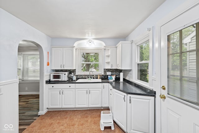 1739 Caldwell Pl, Columbus, IN 47201 - kitchen featuring white microwave, dark countertops, white cabinetry, arched walkways, and decorative backsplash
