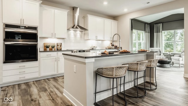 5002 Jasper Ridge Blvd, Indianapolis, IN 46235 - kitchen featuring wall chimney exhaust hood, double oven, light wood-style floors, dark countertops, and recessed lighting