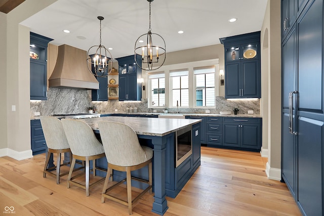 12839 Bird Cage, Carmel, IN 46032 - kitchen with custom range hood, blue cabinetry, a chandelier, a kitchen island, and tasteful backsplash
