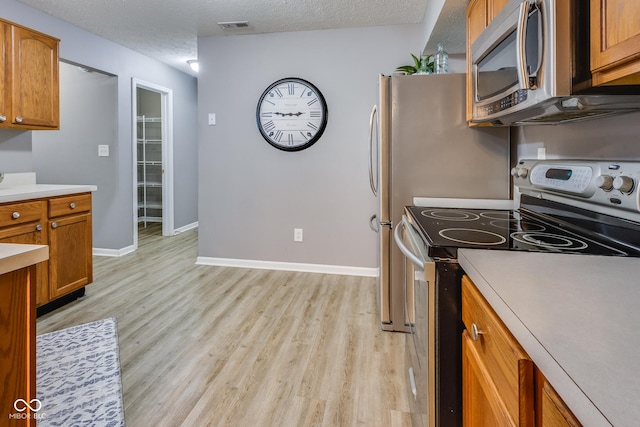 2289 Salem Park Dr, Indianapolis, IN 46239 - kitchen with stainless steel appliances, brown cabinetry, light wood-style flooring, and a textured ceiling