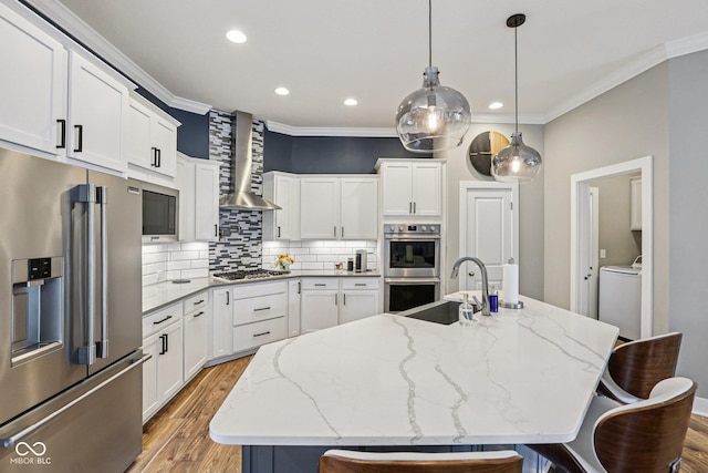 2105 Granville Dr, Westfield, IN 46074 - kitchen featuring stainless steel appliances, wall chimney range hood, a kitchen breakfast bar, crown molding, and light wood finished floors
