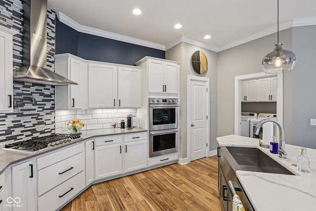 2105 Granville Dr, Westfield, IN 46074 - kitchen featuring washer and dryer, appliances with stainless steel finishes, wall chimney exhaust hood, crown molding, and white cabinetry