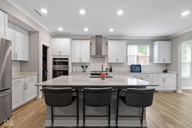 15546 Senita Ln, Fishers, IN 46037 - kitchen with wall chimney exhaust hood, appliances with stainless steel finishes, a breakfast bar area, an island with sink, and crown molding