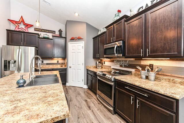 561 Farnham Dr, Westfield, IN 46074 - kitchen featuring appliances with stainless steel finishes, vaulted ceiling, dark brown cabinetry, tasteful backsplash, and light wood-style floors