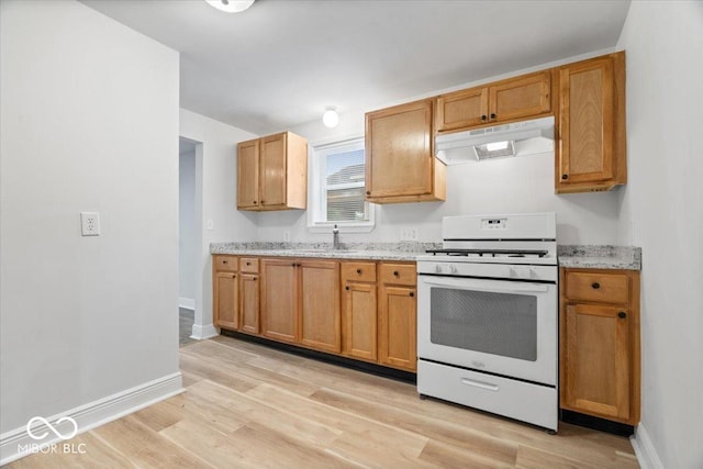4310 Crittenden Ave, Indianapolis, IN 46205 - kitchen featuring under cabinet range hood, white range with gas stovetop, light wood-type flooring, and light stone countertops