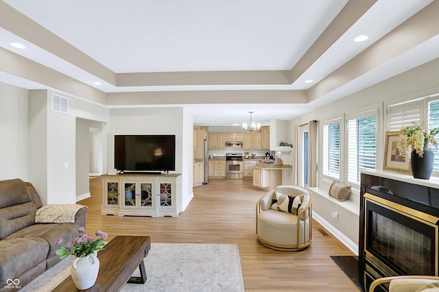 6050 Acorn Dr, Columbus, IN 47201 - living area featuring a tray ceiling, recessed lighting, a fireplace with flush hearth, light wood finished floors, and a chandelier