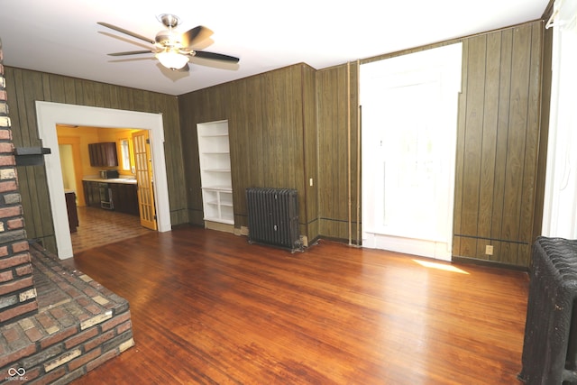 611 E Wabash Ave, Crawfordsville, IN 47933 - unfurnished living room with radiator, ceiling fan, wood walls, wood finished floors, and built in features