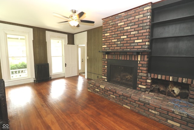 611 E Wabash Ave, Crawfordsville, IN 47933 - unfurnished living room featuring radiator heating unit, a ceiling fan, a fireplace, and wood finished floors