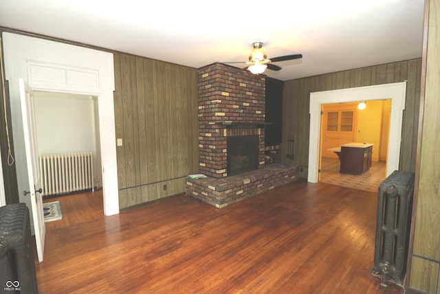 611 E Wabash Ave, Crawfordsville, IN 47933 - unfurnished living room with radiator, a ceiling fan, wood finished floors, a fireplace, and wooden walls