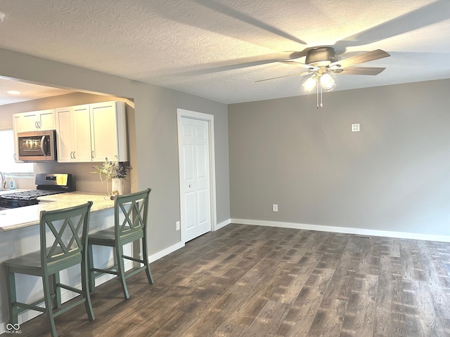 712 W Main St, Thorntown, IN 46071 - kitchen with stainless steel appliances, dark wood-style floors, ceiling fan, white cabinetry, and a kitchen breakfast bar