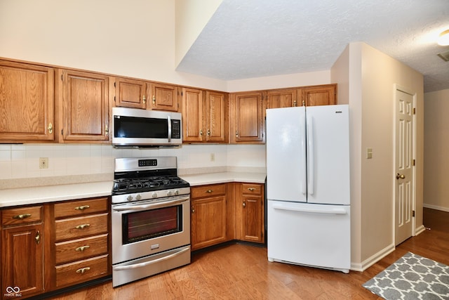 6965 Steinmeier Dr W, Indianapolis, IN 46220 - kitchen featuring appliances with stainless steel finishes, brown cabinetry, light wood finished floors, light countertops, and a textured ceiling