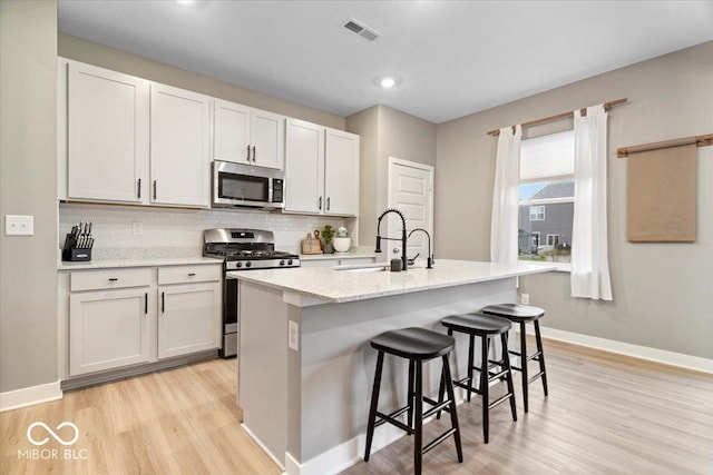 8547 Winton Pl, Pendleton, IN 46064 - kitchen featuring stainless steel appliances, light wood finished floors, decorative backsplash, a kitchen breakfast bar, and a kitchen island with sink