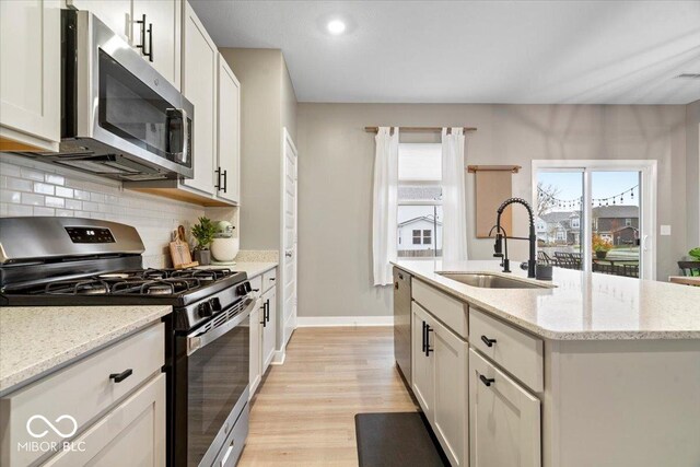 8547 Winton Pl, Pendleton, IN 46064 - kitchen featuring stainless steel appliances, decorative backsplash, light wood finished floors, an island with sink, and light stone counters