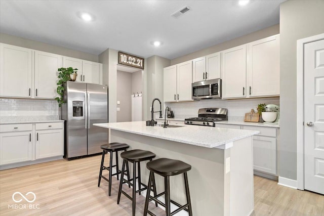 8547 Winton Pl, Pendleton, IN 46064 - kitchen featuring appliances with stainless steel finishes, decorative backsplash, light wood-style floors, a kitchen breakfast bar, and a kitchen island with sink