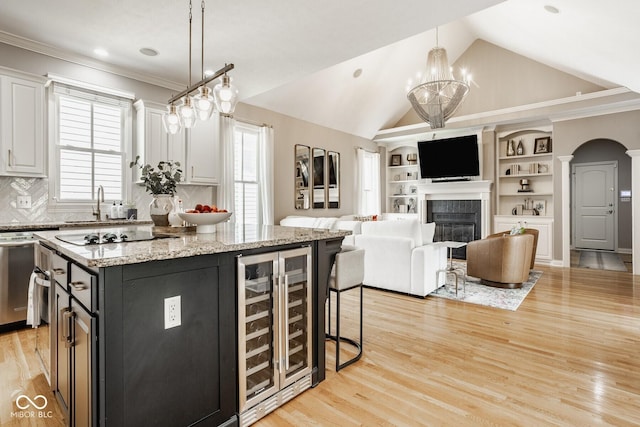 12505 Branford St, Carmel, IN 46032 - kitchen with wine cooler, stovetop, white cabinets, a glass covered fireplace, and arched walkways