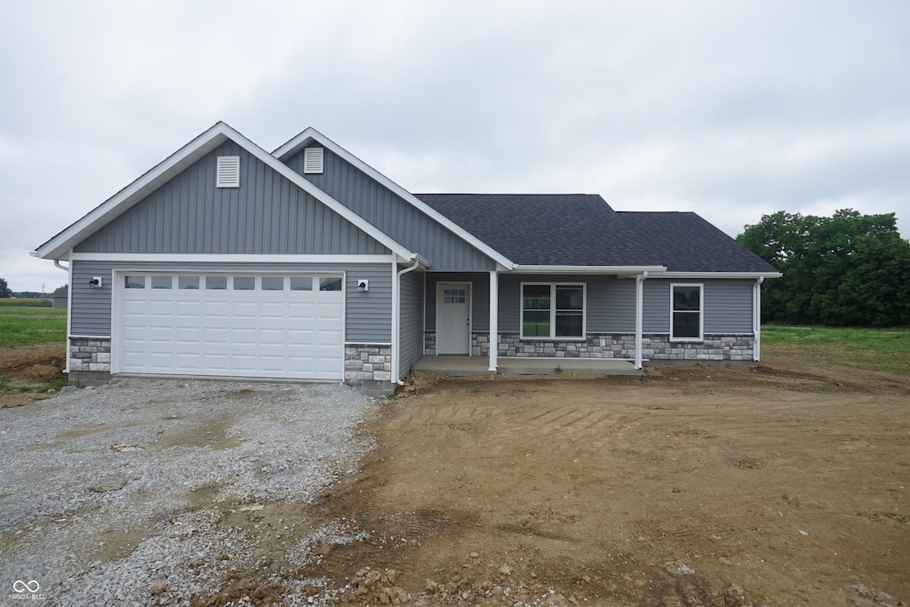583 Shawnee Trl, Milan, IN 47031 - view of front of house with stone siding, a porch, an attached garage, and dirt driveway