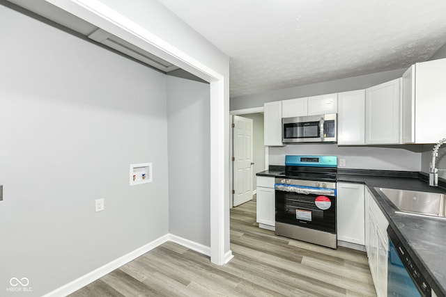 2413 Fowler St, Anderson, IN 46012 - kitchen featuring appliances with stainless steel finishes, white cabinets, dark countertops, light wood-type flooring, and a textured ceiling