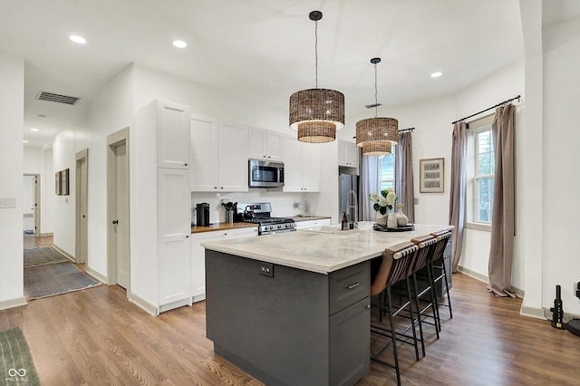 1046 N Hamilton Ave, Indianapolis, IN 46201 - kitchen with appliances with stainless steel finishes, white cabinetry, wood finished floors, a kitchen island with sink, and a breakfast bar area
