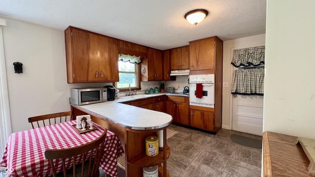 202 Collier St, Columbus, IN 47201 - kitchen with oven, stainless steel microwave, under cabinet range hood, brown cabinetry, and a peninsula
