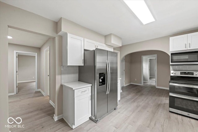 508 W 38th St, Indianapolis, IN 46208 - kitchen featuring stainless steel appliances, arched walkways, decorative backsplash, white cabinets, and light countertops