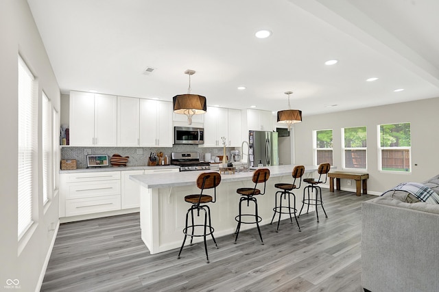 4132 Tincher Rd, Indianapolis, IN 46221 - kitchen featuring stainless steel appliances, backsplash, an island with sink, light wood finished floors, and light countertops