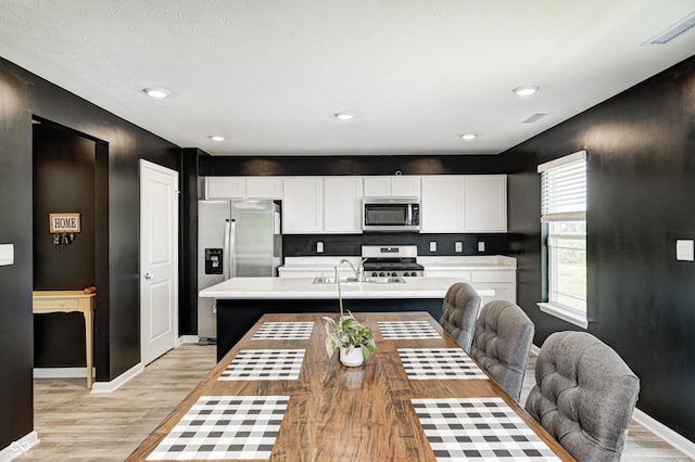 6332 Card Blvd, Indianapolis, IN 46221 - kitchen featuring appliances with stainless steel finishes, light wood-style flooring, light countertops, white cabinets, and a kitchen island with sink